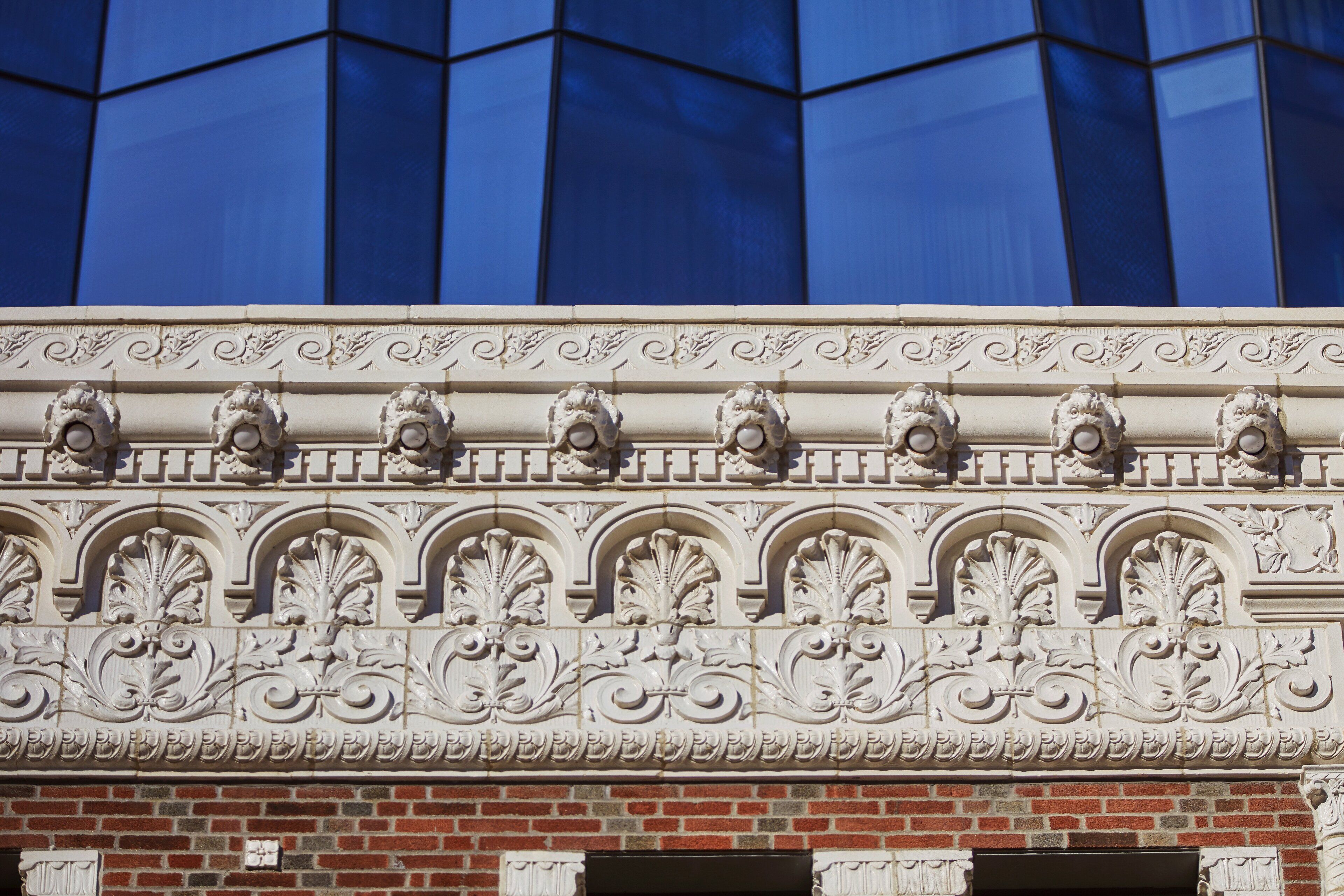 En bygnings facade med udsøgte arkitektoniske detaljer, herunder udskårne stendekorationer og en murstenssokkel.