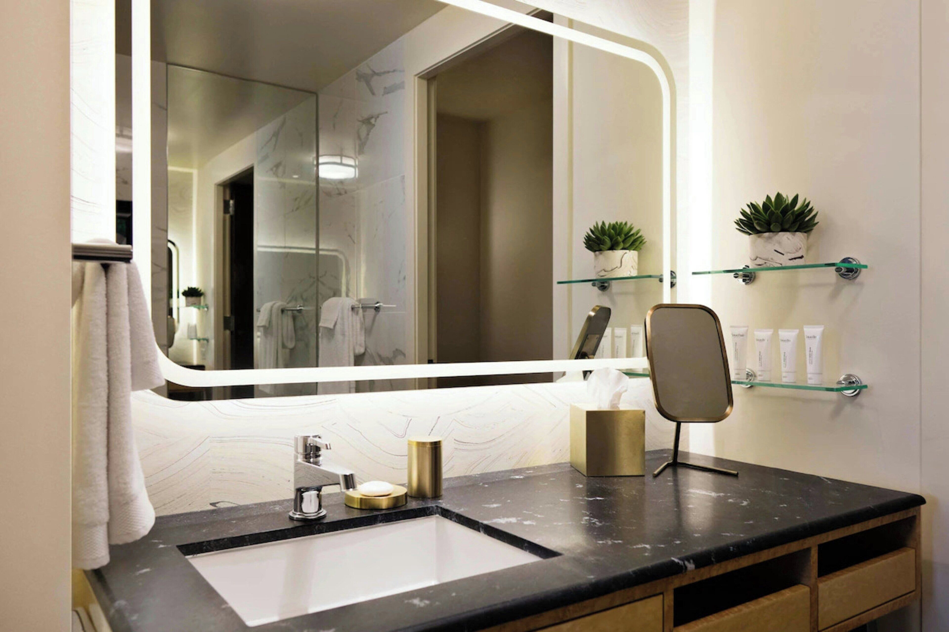 A bathroom with a large mirror, a sink, a towel rack, and two potted plants on shelves.