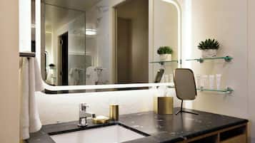 A bathroom with a large mirror, a sink, a towel rack, and two potted plants on shelves.