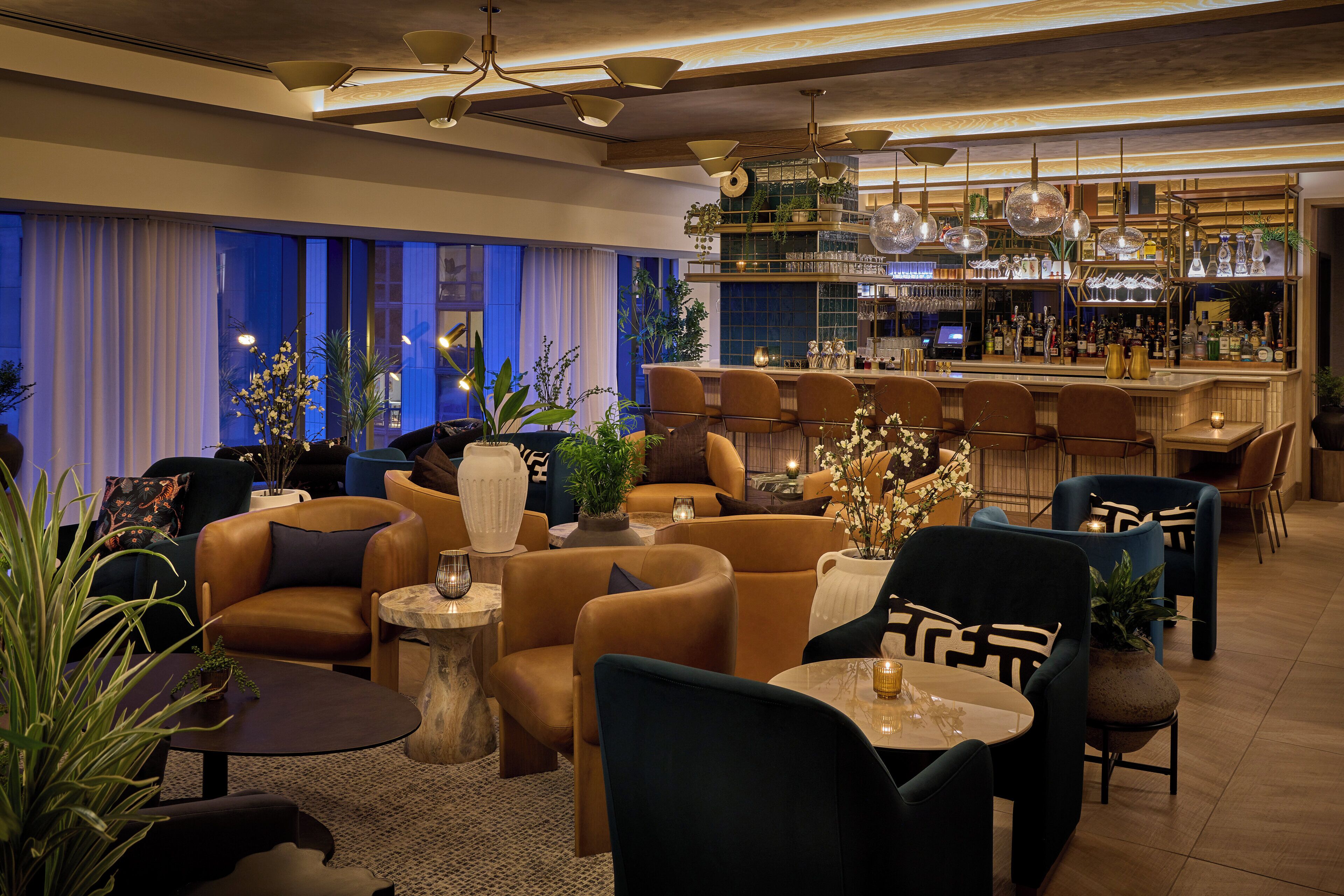 A modern lounge area with leather sofas, round tables, and a bar with shelves of bottles and glasses.