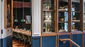A dining area with a long table set for four, green chairs, hanging green pendant lights, and a blue and white cabinet with glass doors displaying decorative items.