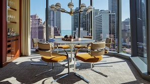 A modern dining area with a round table and chairs, large windows with a city view, and a decorative light fixture. - Viceroy Chicago (Chicago)