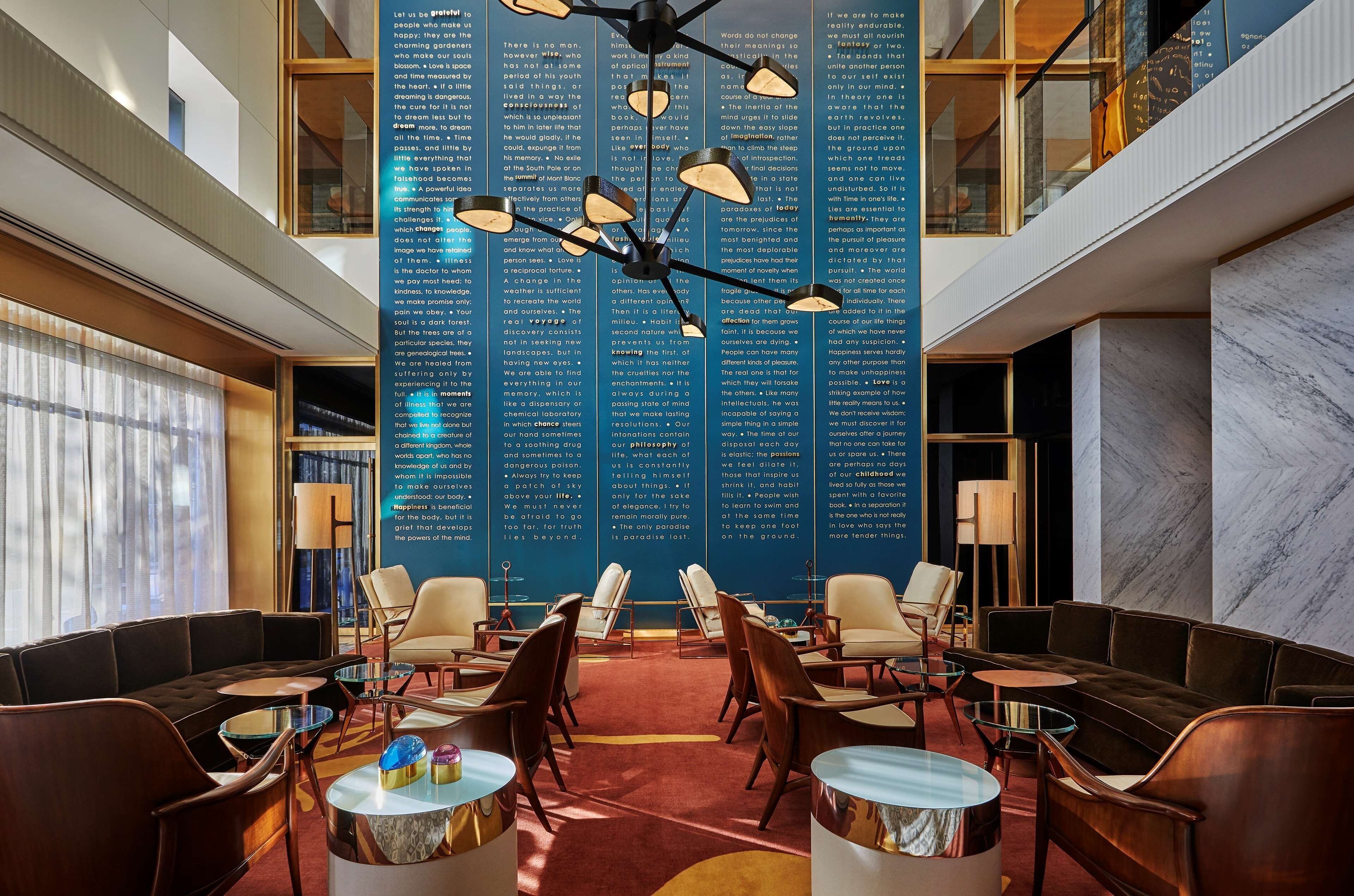 Un hall d’entrée avec un plafond haut, un lustre, des espaces de détente et un grand mur orné de texte.