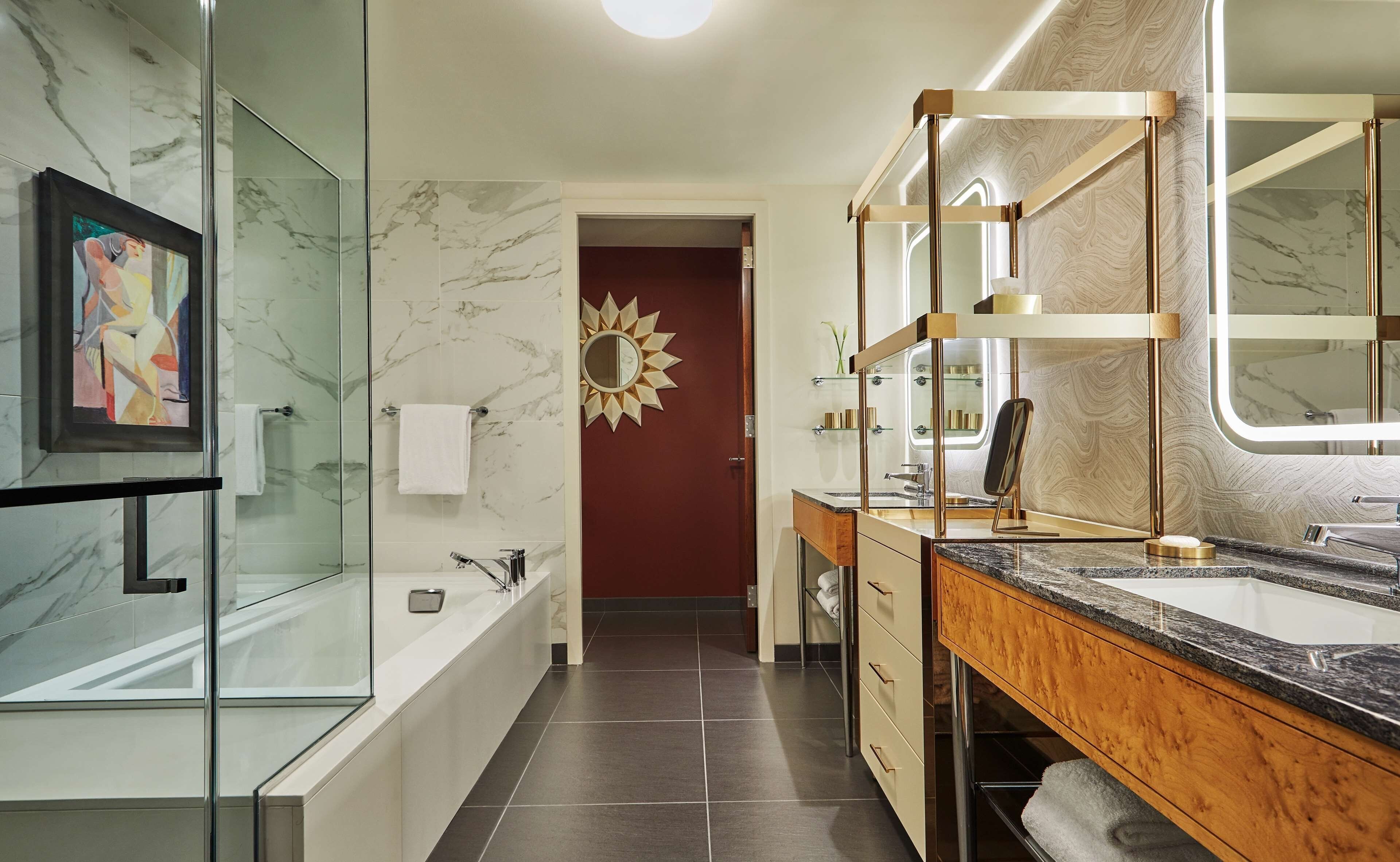 Un baño moderno con ducha de vidrio, bañera, tocador con un espejo grande y decoración de pared con forma de sol.