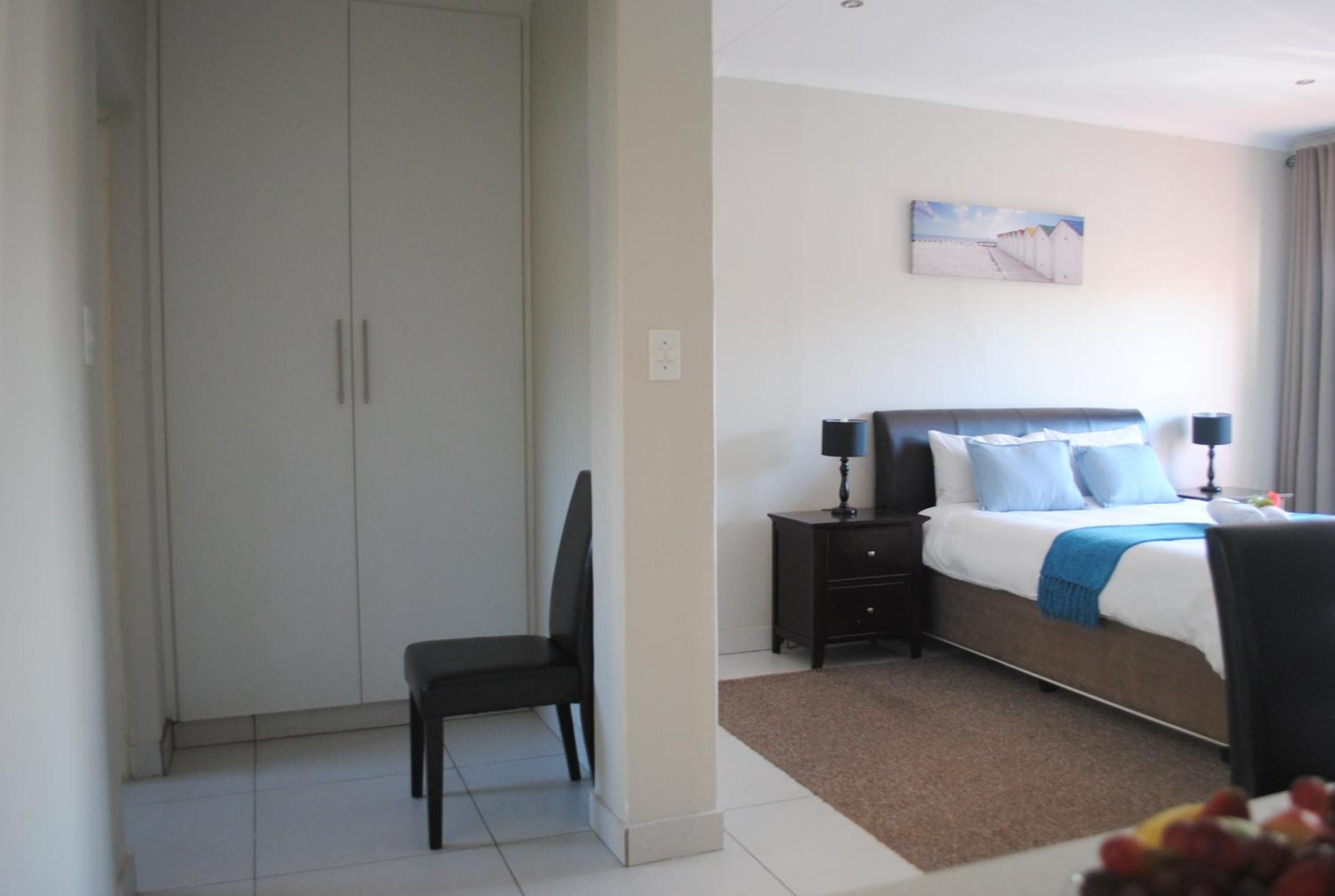 A bedroom with a bed, bedside tables, a chair, a wardrobe, and a painting on the wall.