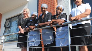 A group of people standing on a balcony with a metal railing, a brick wall, and a window with blinds. - 86 Edison Guest Lodge (Sandton)