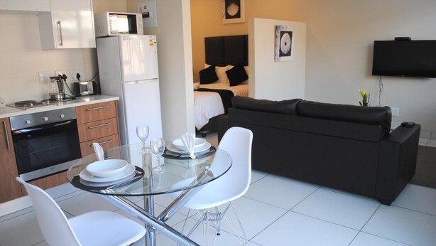 A compact living space with a kitchenette, dining area, and a sofa. - 86 Edison Guest Lodge (Sandton)