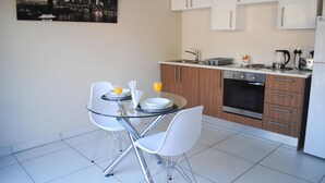 A modern kitchen with white cabinets, a stainless steel oven, and a dining area with a glass table and white chairs. - 86 Edison Guest Lodge (Sandton)