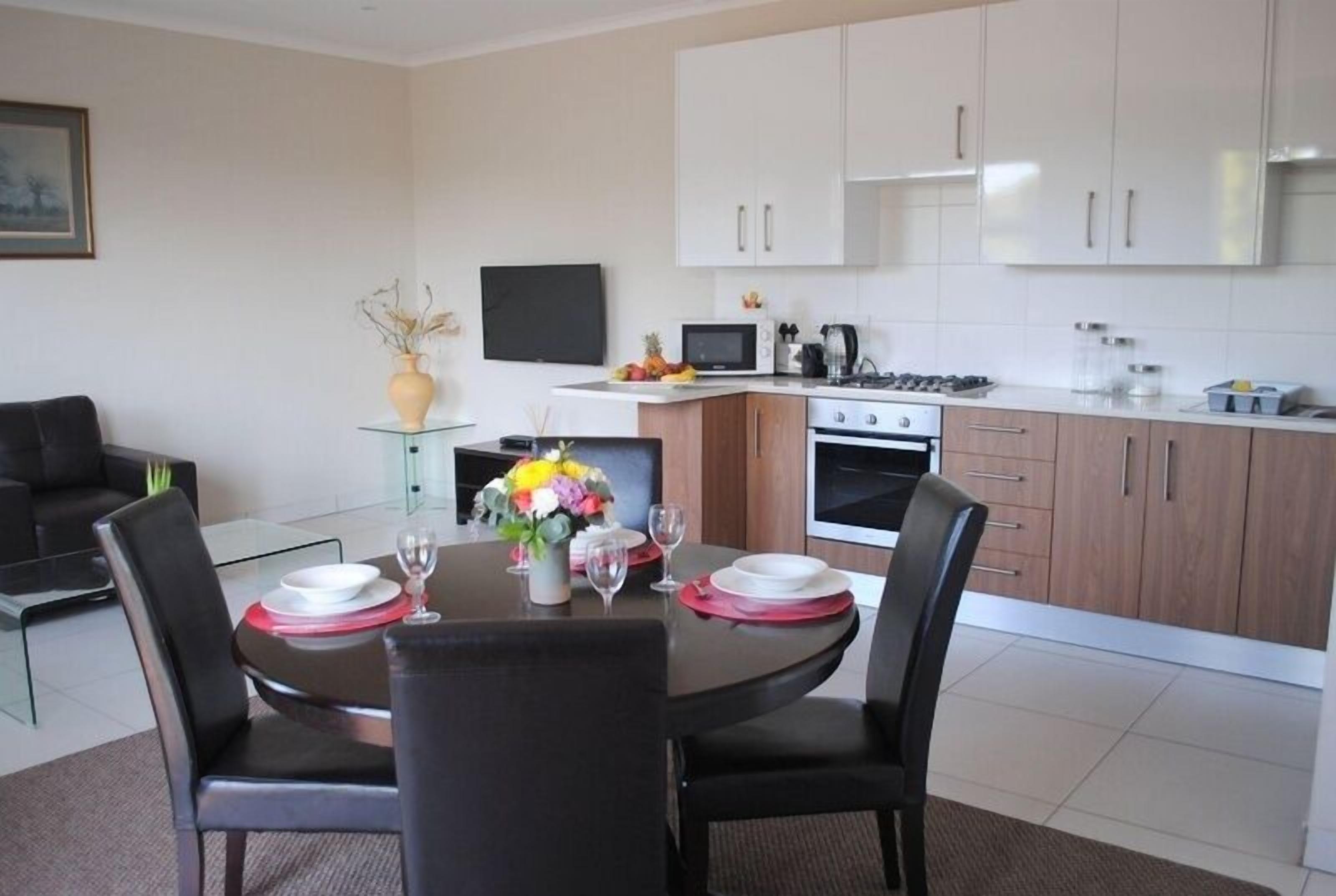 A modern kitchen with white cabinets, a dining table set for four, and a flat-screen TV mounted above the counter.