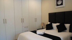 A hotel room with a large bed, a nightstand with a lamp, and a wardrobe with multiple doors. - 86 Edison Guest Lodge (Sandton)