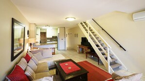 En stue med sofa, sofabord og fjernsyn. Der er en trappe til en etage ovenpå.