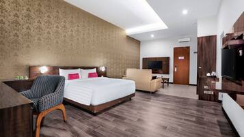 A hotel room with a large bed, a desk, a chair, a TV, and a wardrobe.