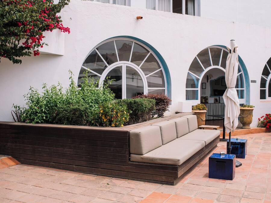 Un patio con un banco integrado, plantas en macetas y un paraguas blanco.