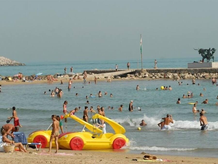 A beach with people swimming and playing, a lifeguard tower, and a statue.