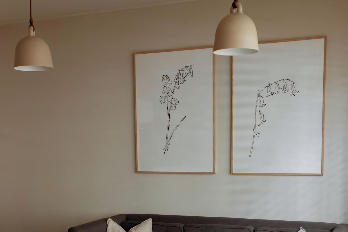 Ein modernes Wohnzimmer mit einem dunkelgrauen Sofa, zwei gerahmten Pflanzenbildern an der Wand, einem weißen Couchtisch und einem runden Hocker.