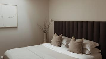 A bedroom with a large bed, a skylight, a wall-mounted artwork, and a vase with branches.