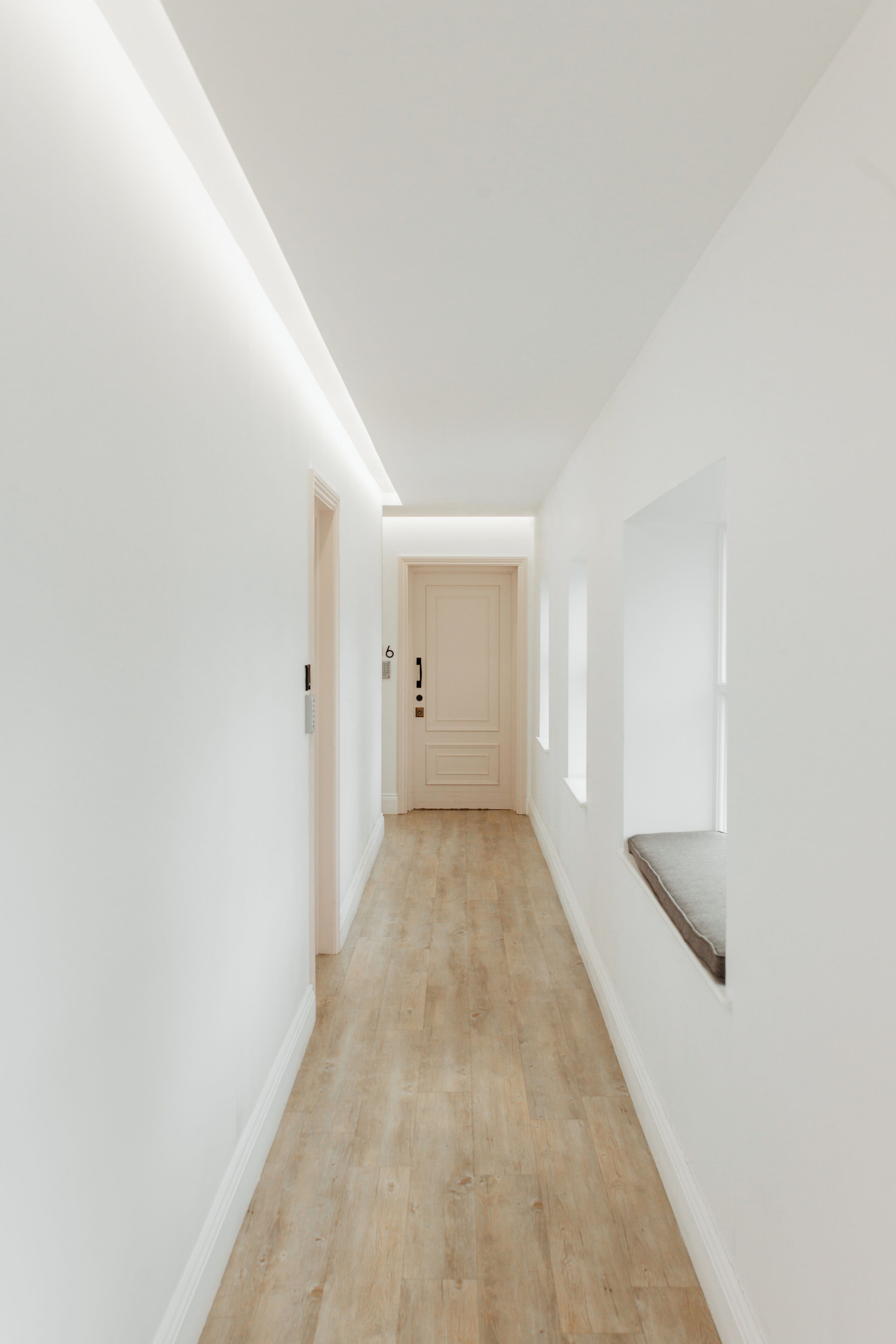 A narrow, well-lit hallway with wooden flooring and white walls.
