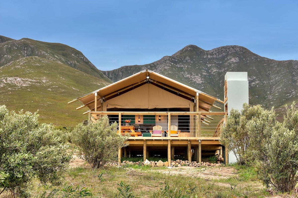 A wooden cabin with a balcony, surrounded by mountains and sparse vegetation.