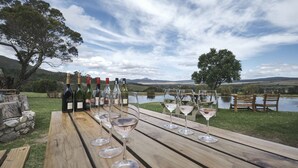 A wooden table with wine bottles and glasses, overlooking a lake and hills. - AfriCamps at Stanford Hills Estate- Glamping (Stanford)