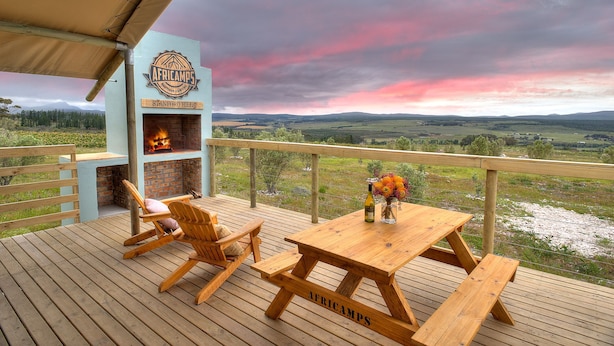 A wooden deck with a brick fireplace, outdoor seating, and a view of the landscape. - AfriCamps at Stanford Hills Estate- Glamping (Stanford)