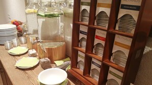 A buffet setup with various tea options, a water dispenser, and a fruit bowl. - Burg Hotel (Feldberg)