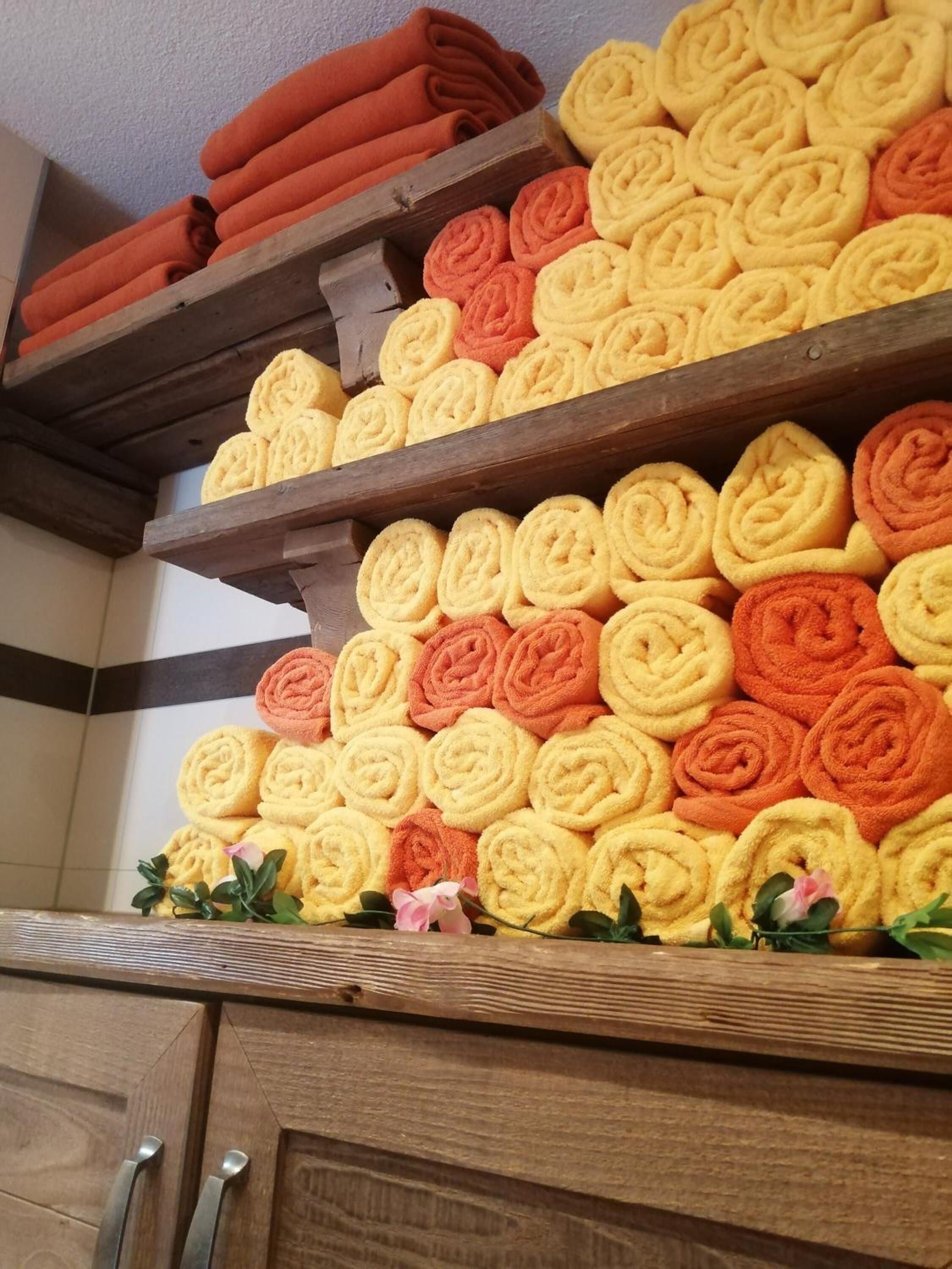 Una estantería de madera con toallas enrolladas ordenadamente en tonos naranja y amarillo.