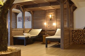 Una cabaña de madera acogedora con dos sillas de mimbre, una mesa pequeña con un vaso, y una lámpara de pared.