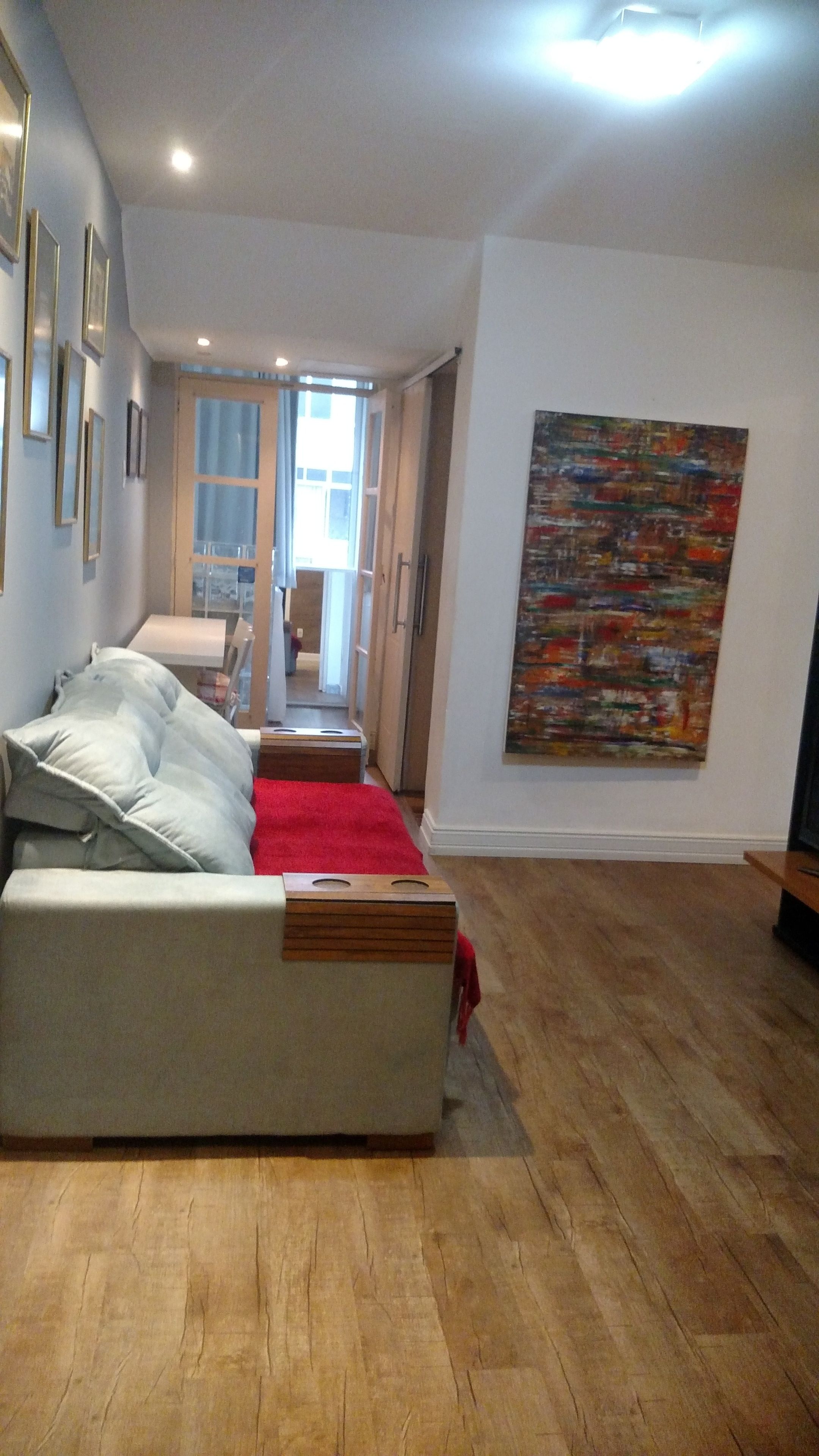 Ein modernes Wohnzimmer mit einer Couch, einer roten Tagesdecke, Holzboden und einem großen abstrakten Gemälde an der Wand.