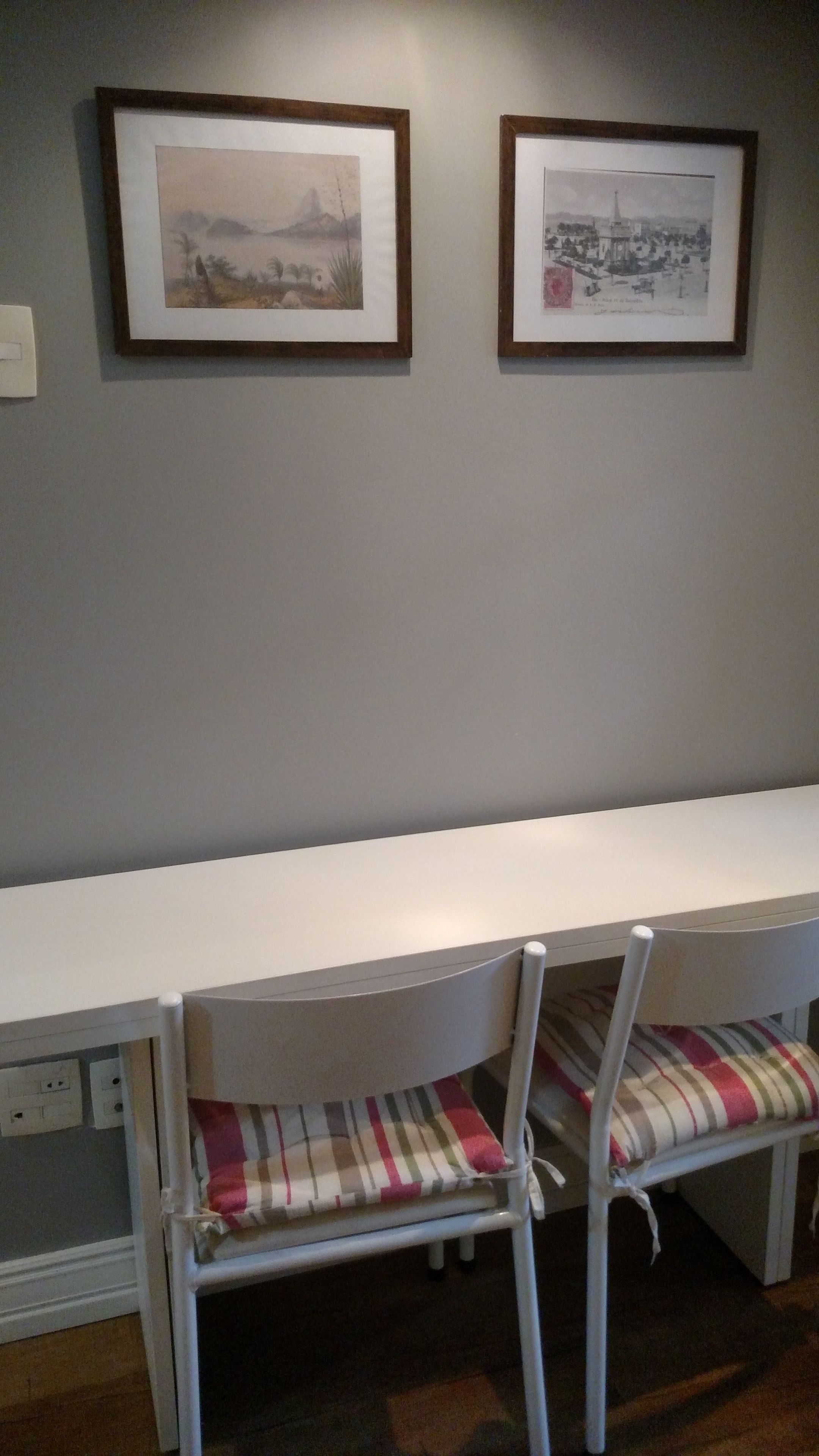 A dining area with a white table and chairs, framed artwork on the wall, and a power outlet on the wall.
