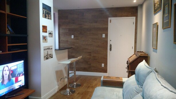 A living room with a TV, a white sofa, a small bar area, and a wooden accent wall. - Copacabana Guest House (Rio de Janeiro)