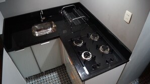 A compact kitchen with a black countertop, a stainless steel sink, and a gas stove with four burners. - Copacabana Guest House (Rio de Janeiro)