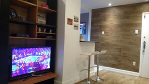 A living room with a flat-screen TV, wooden shelves, a white wall, and a wooden door. - Copacabana Guest House (Rio de Janeiro)