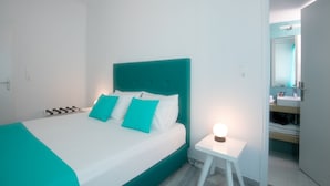 Una habitación de hotel moderna con una cama color turquesa, ropa de cama blanca y una mesita de noche pequeña con una lámpara.