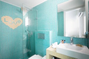 A bathroom with turquoise mosaic tiles, a glass shower enclosure, a sink with a mirror, and a towel rack.