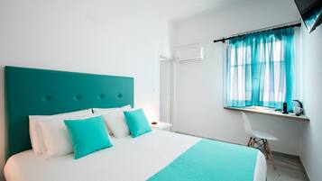 Una habitación de hotel moderna con una cama grande, un escritorio con una silla y un ventanal con cortinas translúcidas.