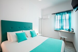 Una habitación de hotel moderna con una cama grande, un escritorio con una silla y un ventanal con cortinas translúcidas.