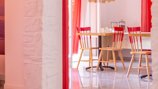 Un área de comedor con una mesa, sillas, una lámpara colgante y cortinas rojas.