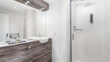 Une salle de bain moderne avec un meuble-lavabo en bois, un grand miroir, une douche en verre et des carreaux blancs.