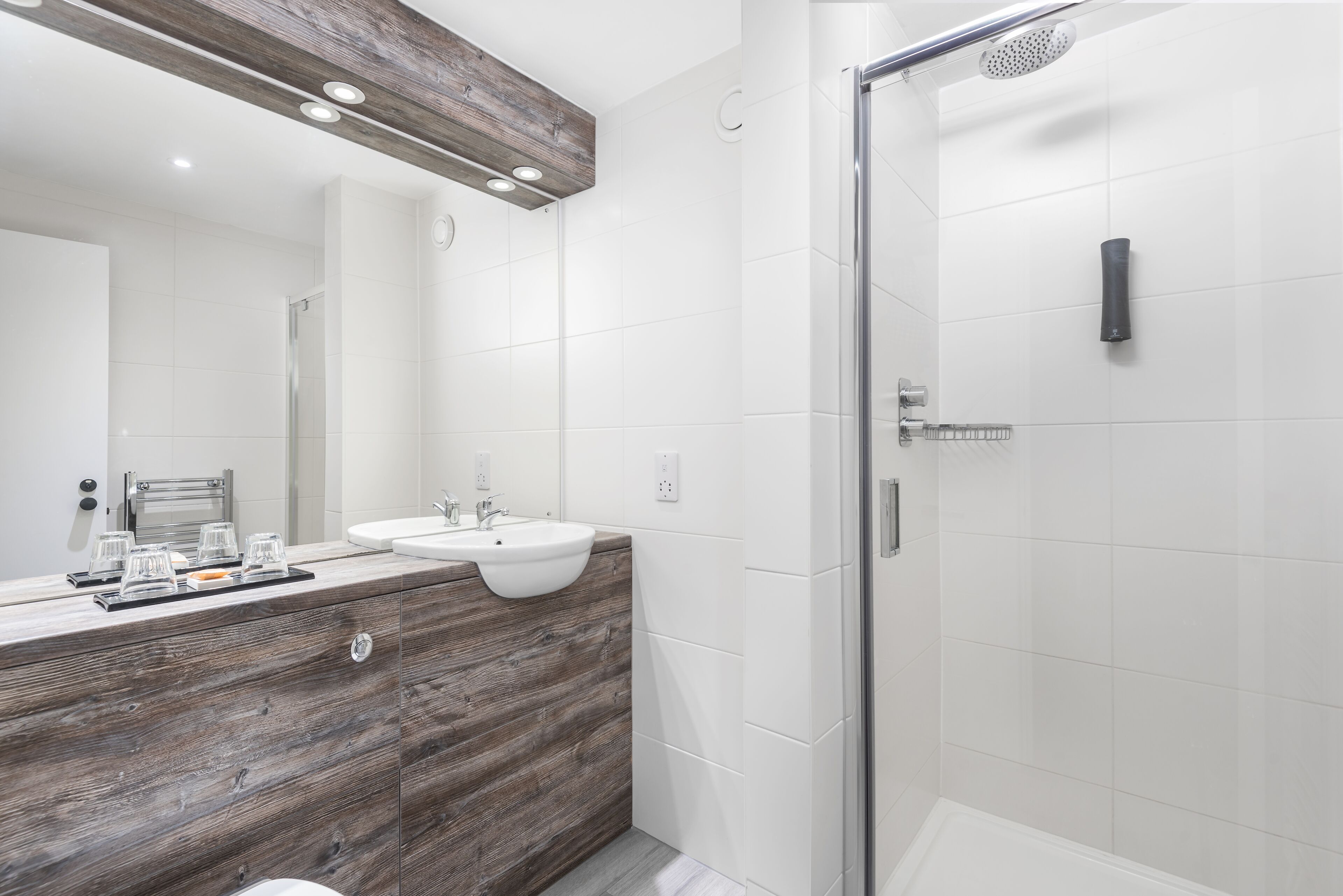 A modern bathroom with a wooden vanity, two sinks, a glass shower enclosure, and a large mirror.
