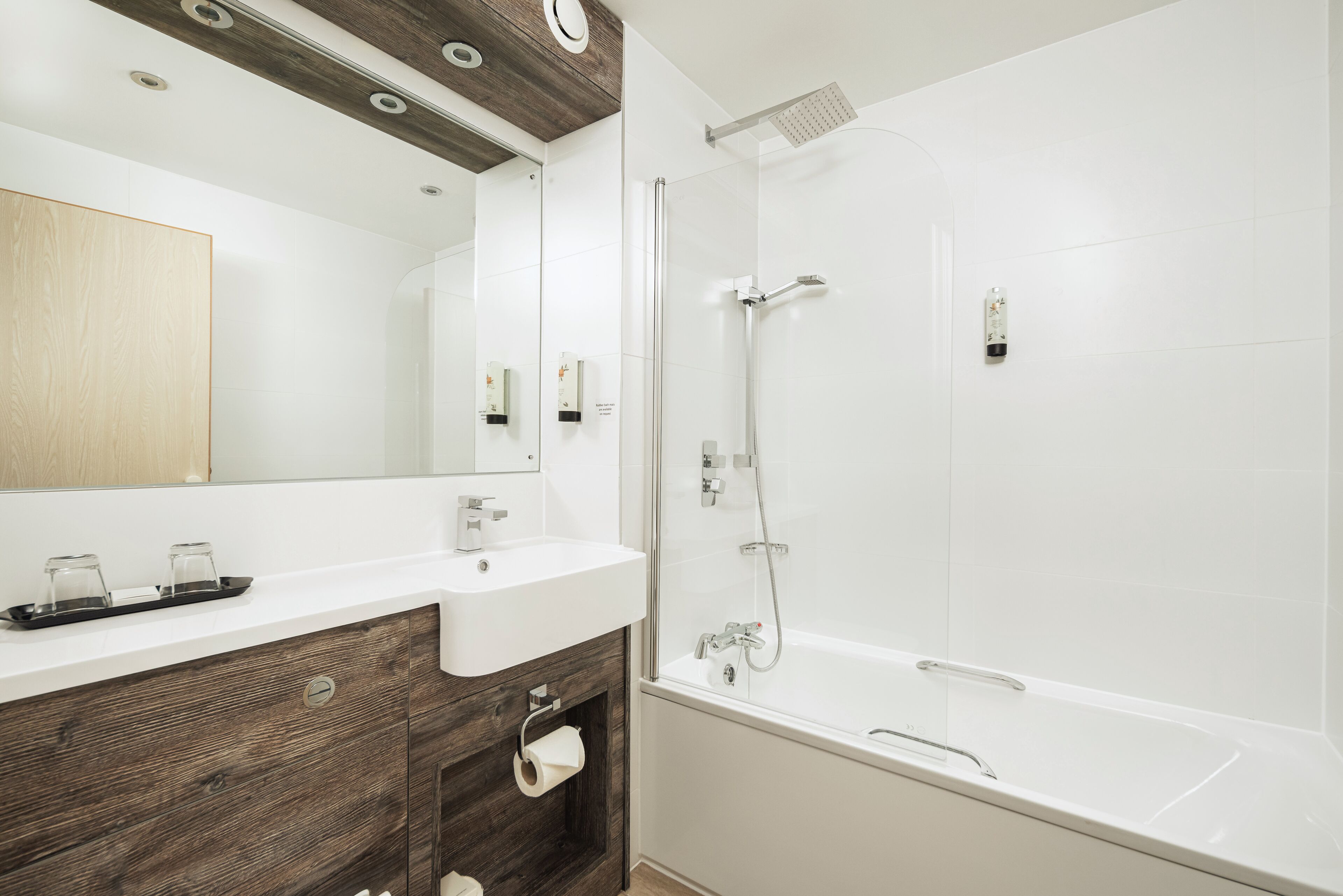 Un baño moderno con tocador de madera, un espejo grande, un lavamanos blanco y cabina de ducha con paredes de vidrio.