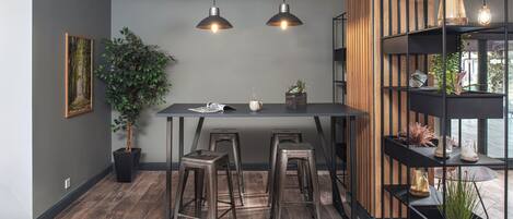 Une cuisine moderne avec un mur d’accent en bois, deux suspensions lumineuses, un bar en métal noir et une plante en pot.