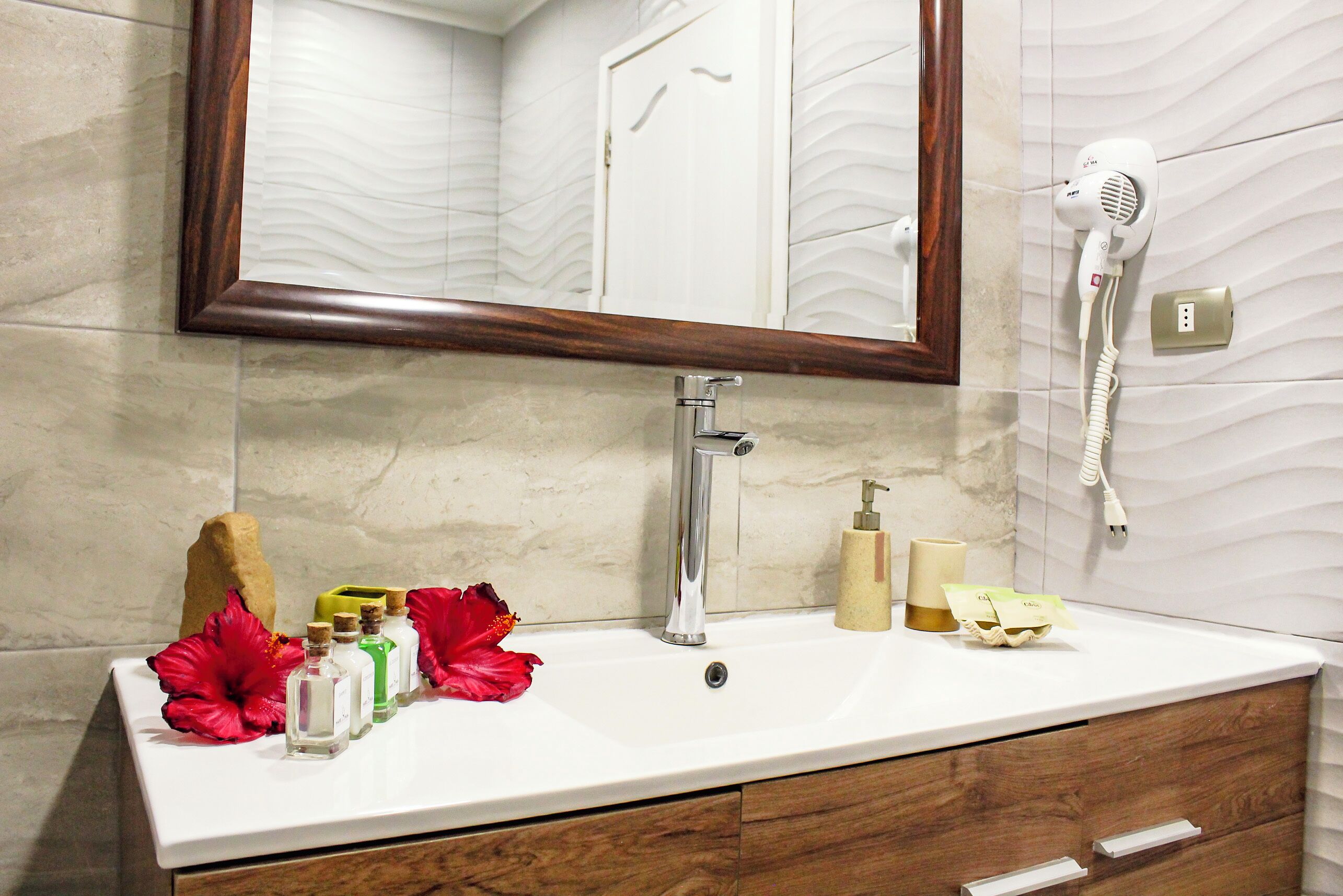 A bathroom with a white sink, a mirror, a hairdryer, and toiletries.