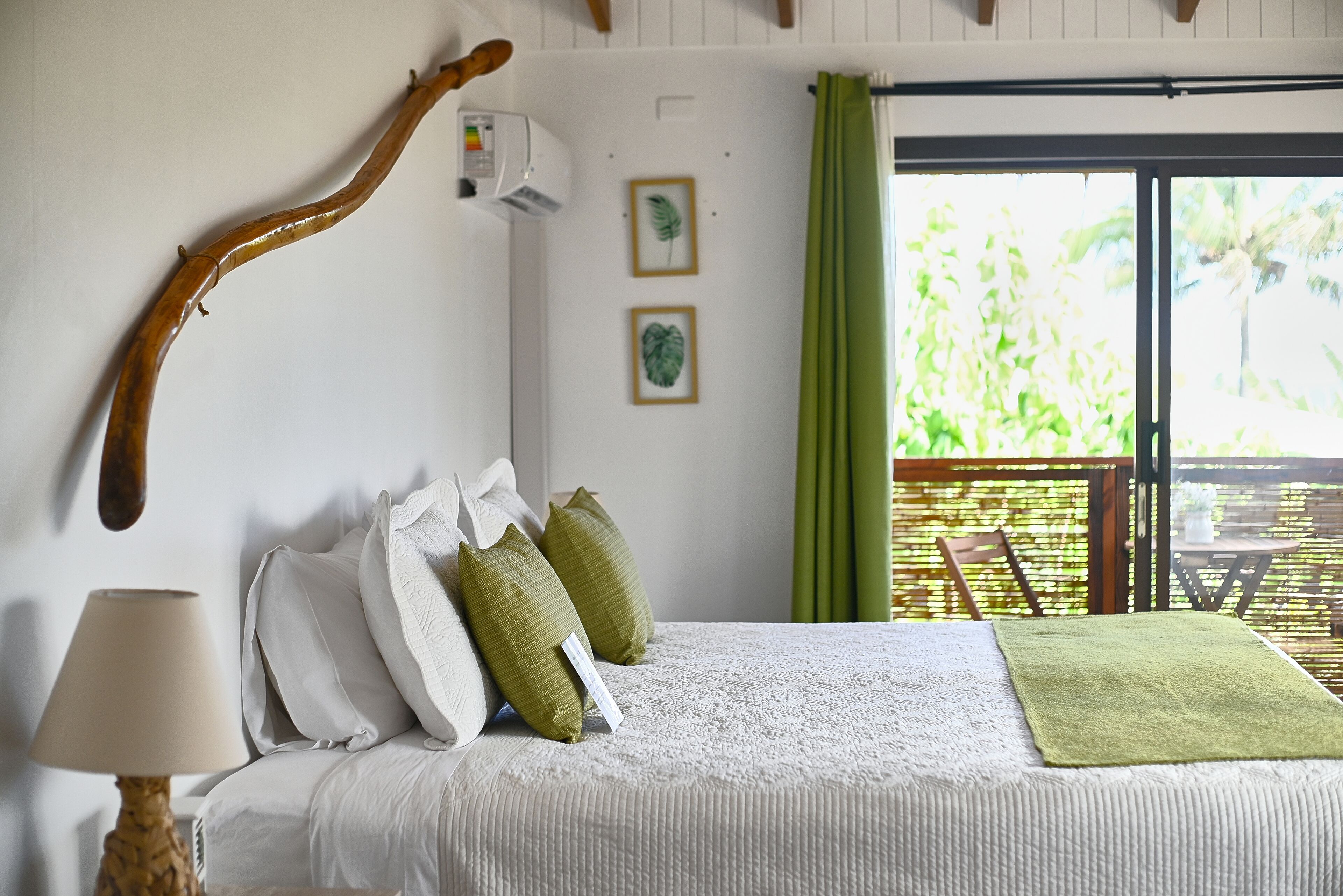 Un dormitorio con cama, almohadas, una lámpara, una rama de madera y vistas al exterior.