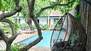 A wooden deck with a hanging chair, a pool, and a building in the background. - Hare Nua (Hanga Roa)