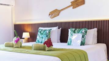 A hotel room with a bed, green towels, a wooden paddle wall decoration, and tropical-themed pillows.