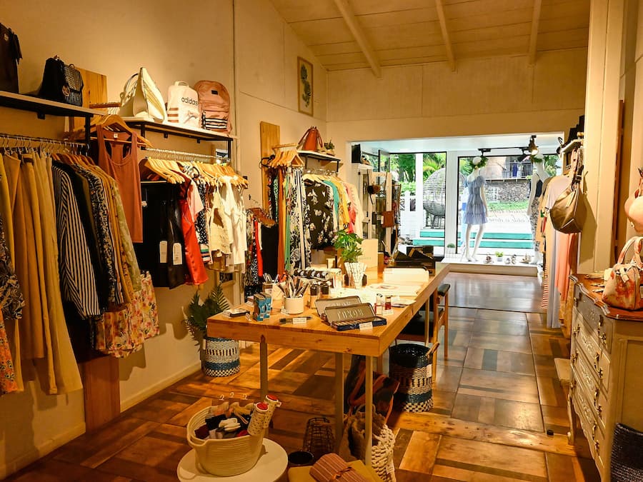 A boutique clothing store with racks of clothes, a wooden table with items, and a view of the outdoors.