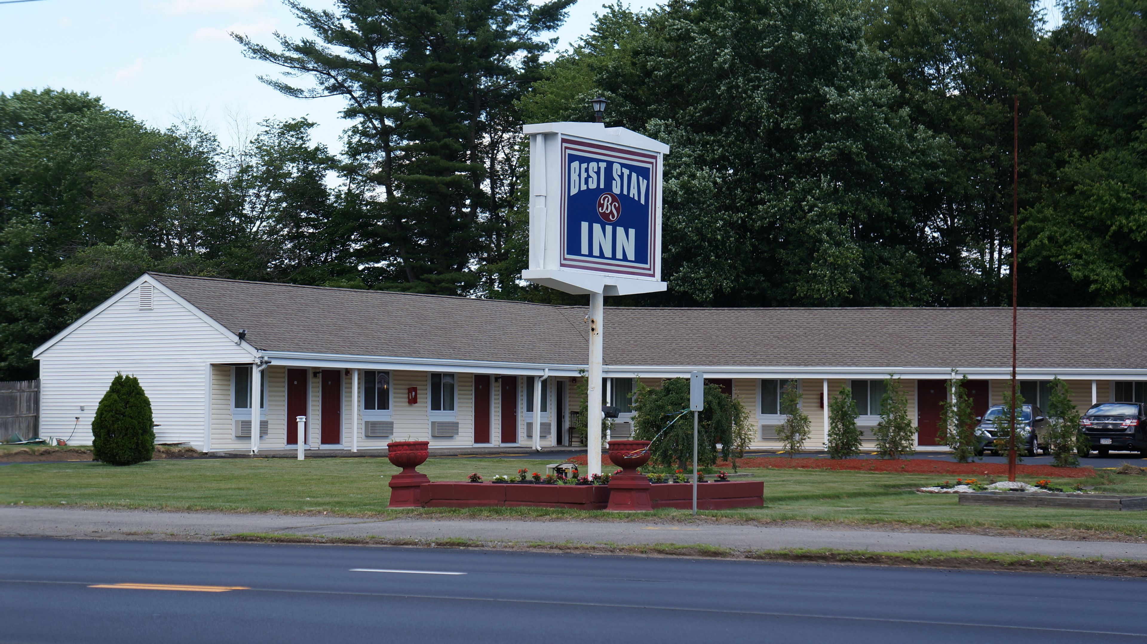 Ein Best Stay Inn mit eingeschossiger Bauweise, überdachtem Parkplatz und einem Rasen mit Pflanzkübeln.