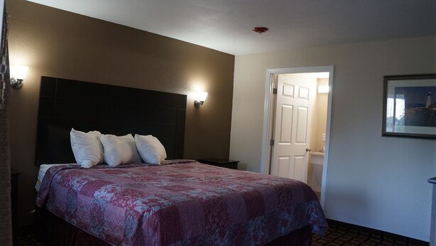 A hotel room with a bed, a nightstand, a wall-mounted lamp, and a door leading to another room. - Best Stay Inn (Plainville)
