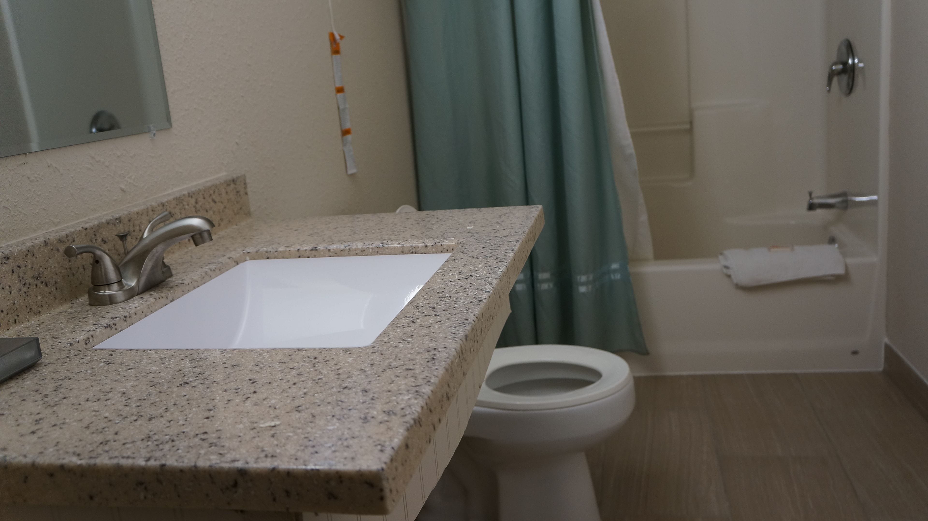 A bathroom with a granite countertop sink, a mirror, a toilet, and a bathtub.