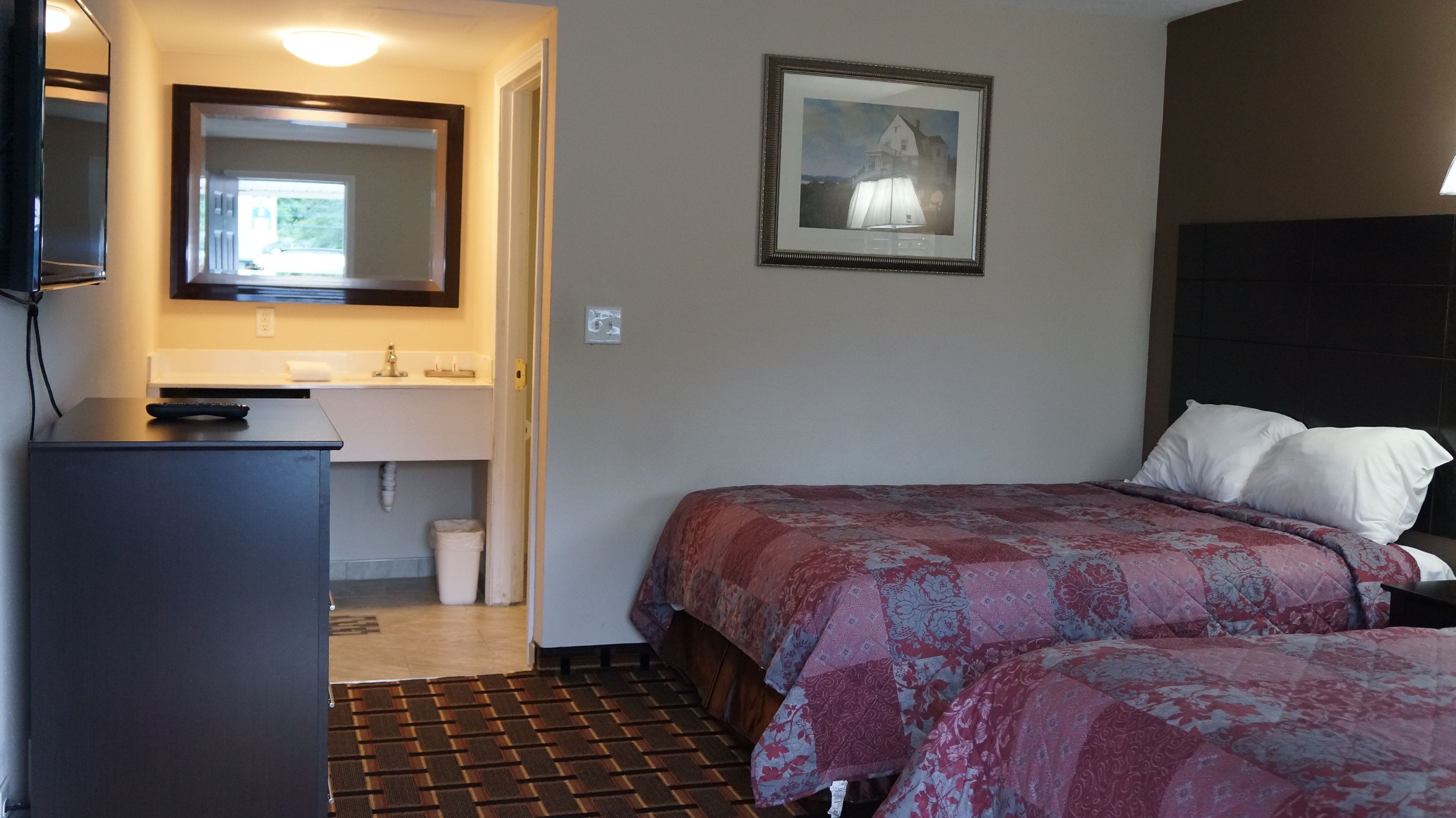 Una camera d'hotel con un letto, una scrivania con un telecomando, un lavandino e un quadro appeso al muro.